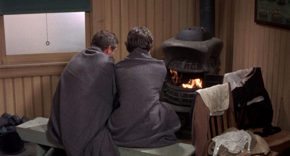 Two people wrapped in blankets by the fireplace