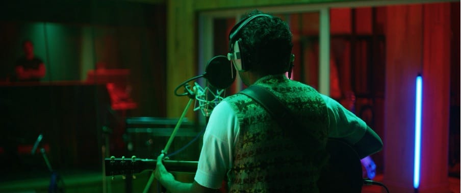 Artist singing in a recording studio, facing a microphone and facing away from the camera