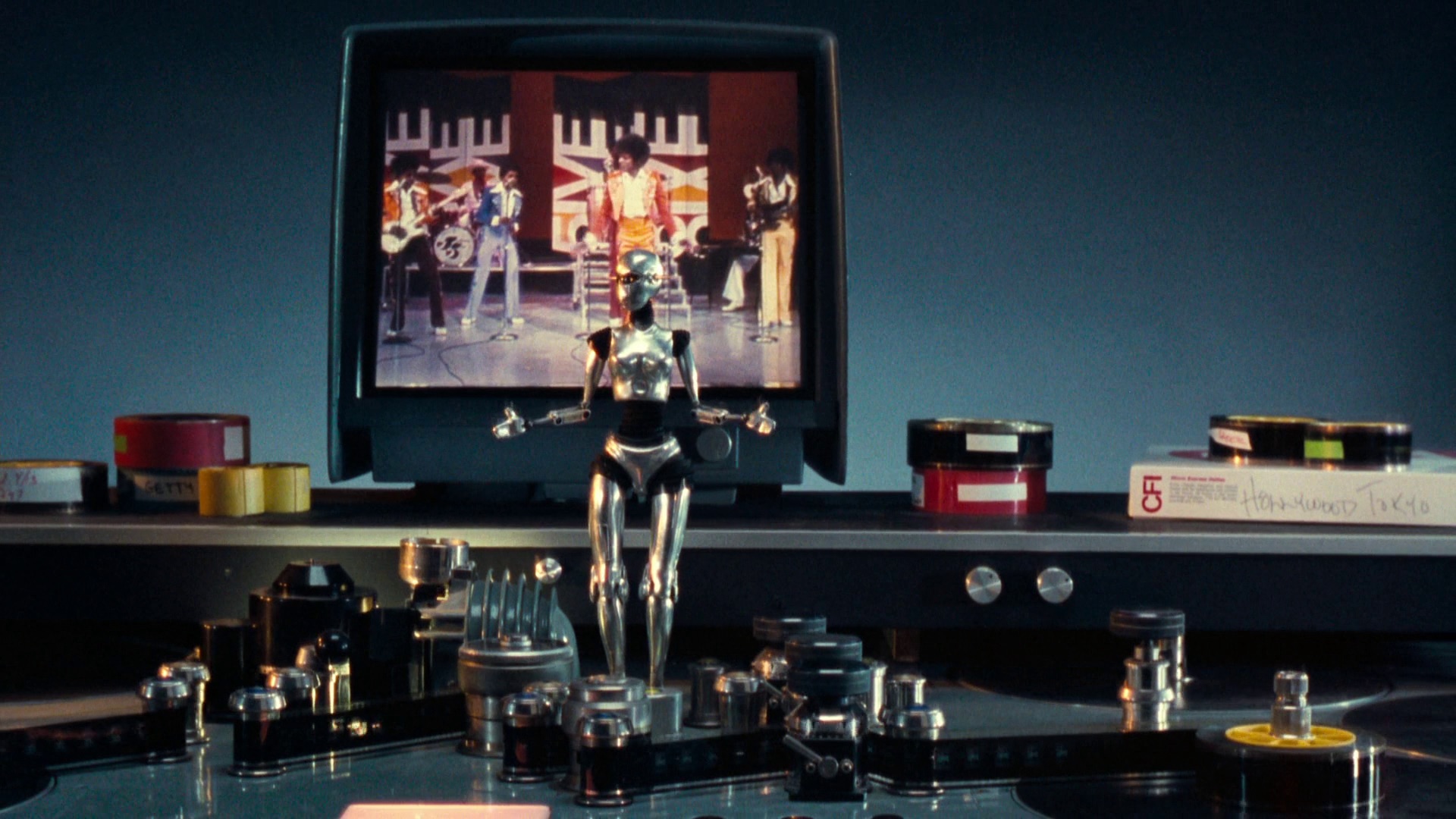 Photo of a small robot dancing in front of a TV with a live band playing